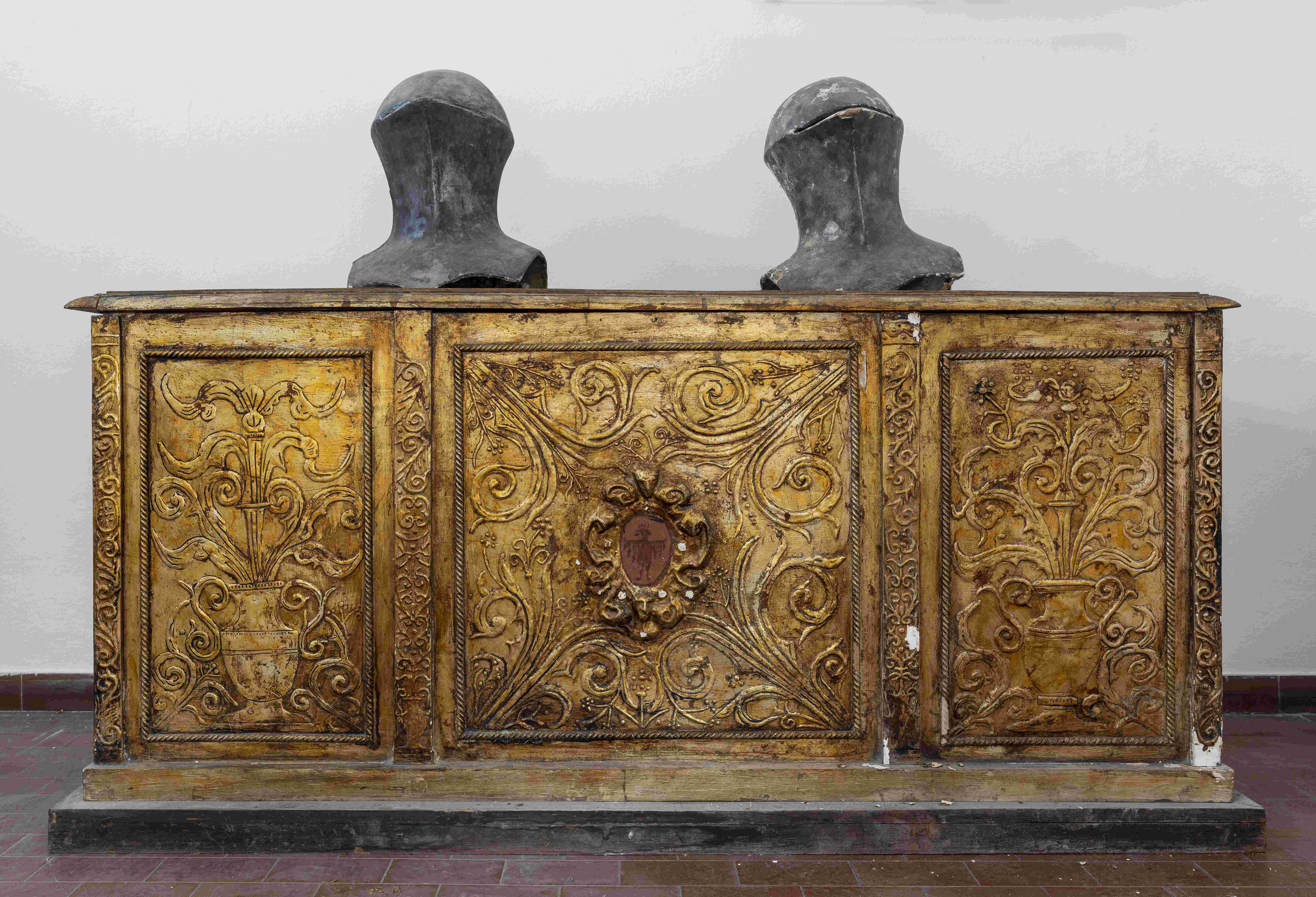 Adalberto Pazzini, grande cassone di legno, decorato a rilievo e dorato. Sopra di esso vi sono due elmi da giostra, in cartapesta dipinta (sempre di mano di Adalberto), facenti parte delle panoplie un tempo appese alle pareti della sala d’armi